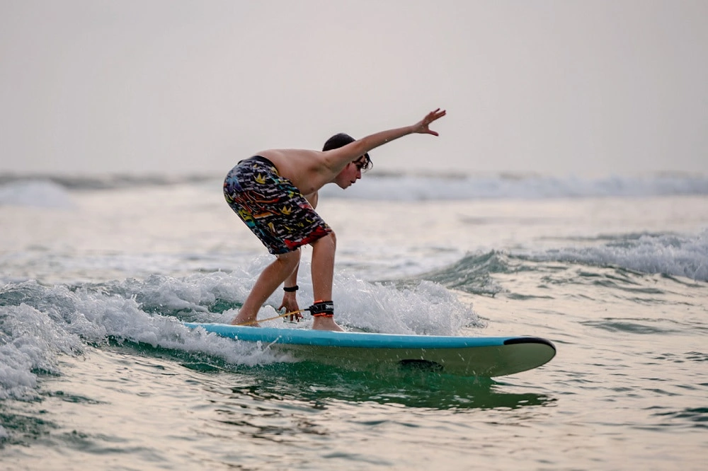 Young male surfer riding waves, surf school in Santa Barbara, California, ocean surfing, beginner surf lessons, coastal activity.